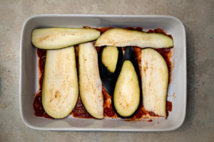 marinara sauce in the bottom of a baking dish topped with slices of eggplant