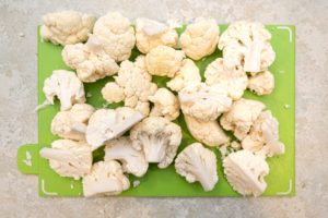 Cauliflower cut into florets on chopping board