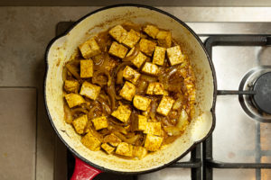 Tofu cooking in frying pan with onions and spices