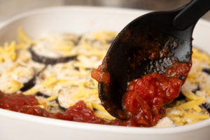 Marinara sauce being spooned onto eggplant parmigiana