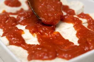 Enchilada sauce poured over enchiladas in baking dish