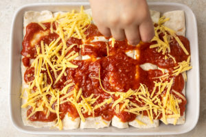 Grated vegan cheese being sprinkled over enchiladas