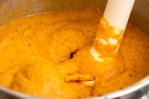 Veggies, stock and coconut milk being blended with a stick blender